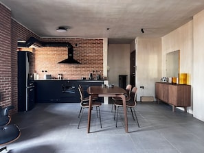 Une cuisine moderne avec un mur de fond en briques, un îlot central et un coin repas comprenant une table et des chaises en bois.