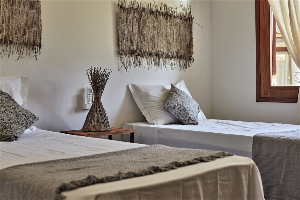 A bedroom with two beds, a bedside table with a vase, and woven wall hangings.