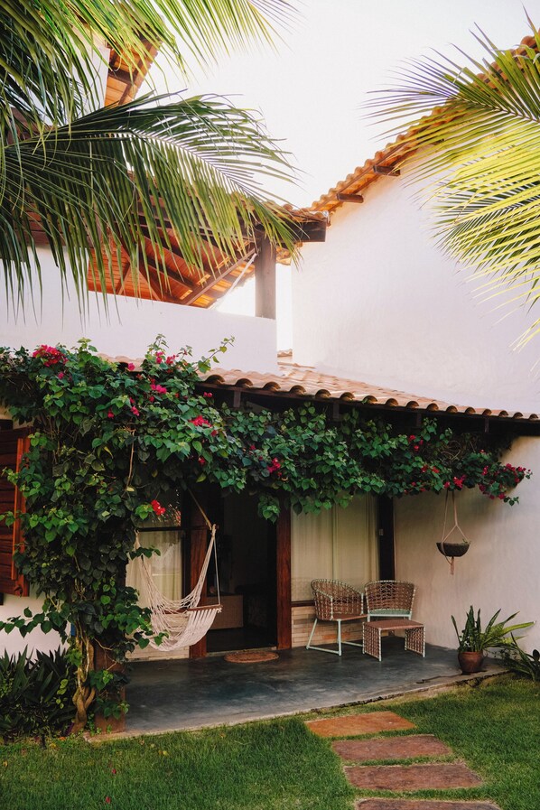 Un patio con una hamaca, dos sillas de mimbre, una planta en maceta y una palmera.