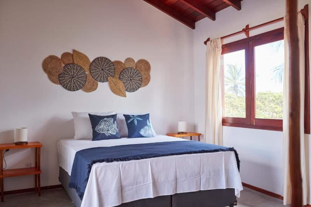 A bedroom with a bed, two bedside tables, a window with curtains, and wall decor.