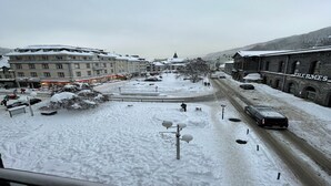 A snow-covered urban area with buildings, a road, and a car. - Bright Apartment in Mont-Dore (Mont-Dore)