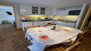 A kitchen with white cabinets, a microwave, and a dining table with a tablecloth. - Bright Apartment in Mont-Dore (Mont-Dore)