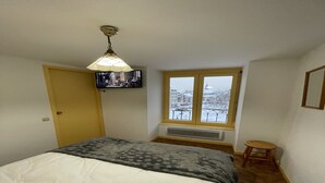 A bedroom with a bed, a television mounted on the wall, a window with a view of a cityscape, and a small stool. - Bright Apartment in Mont-Dore (Mont-Dore)