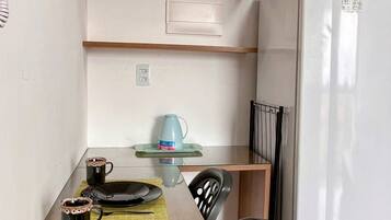 A compact kitchen with a dining table set for two, a refrigerator, and wooden shelves above the counter.
