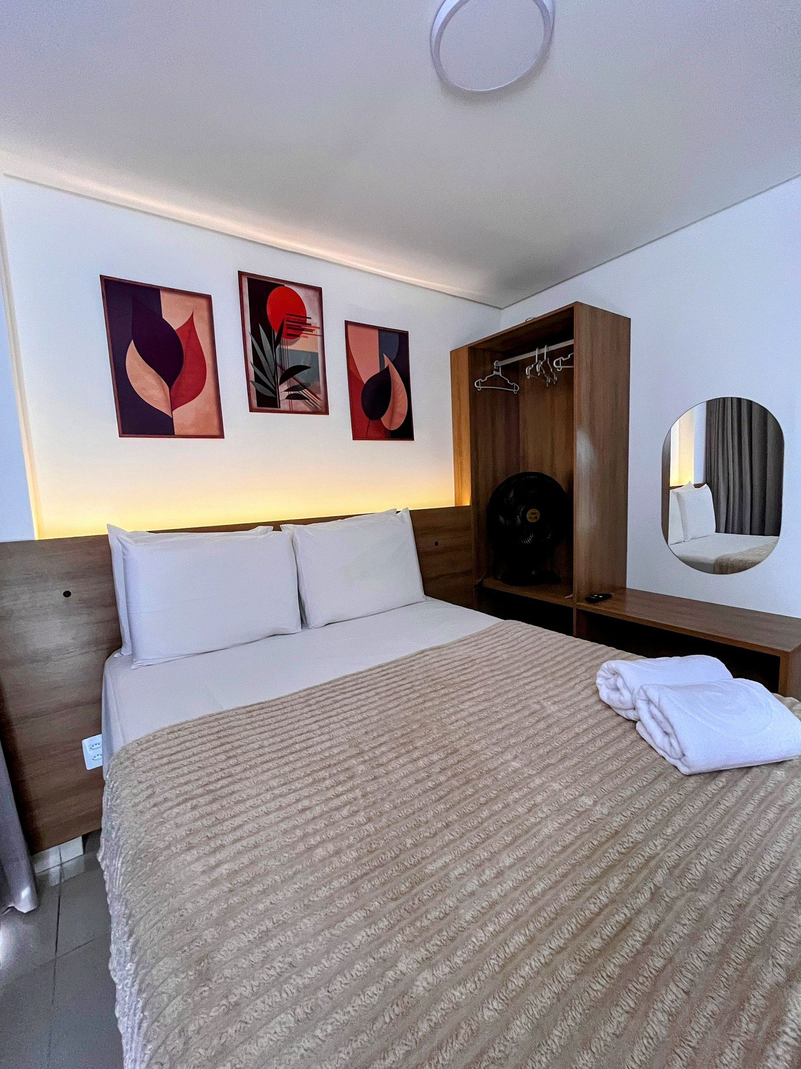 A hotel room with a bed, a wooden wardrobe, a mirror, and abstract wall art.