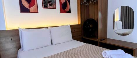 A hotel room with a bed, a wooden wardrobe, a mirror, and abstract wall art.