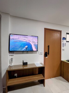 Una habitación con un televisor montado en la pared, una mesita consola de madera, una puerta y un estante pequeño con un teléfono y llaves.