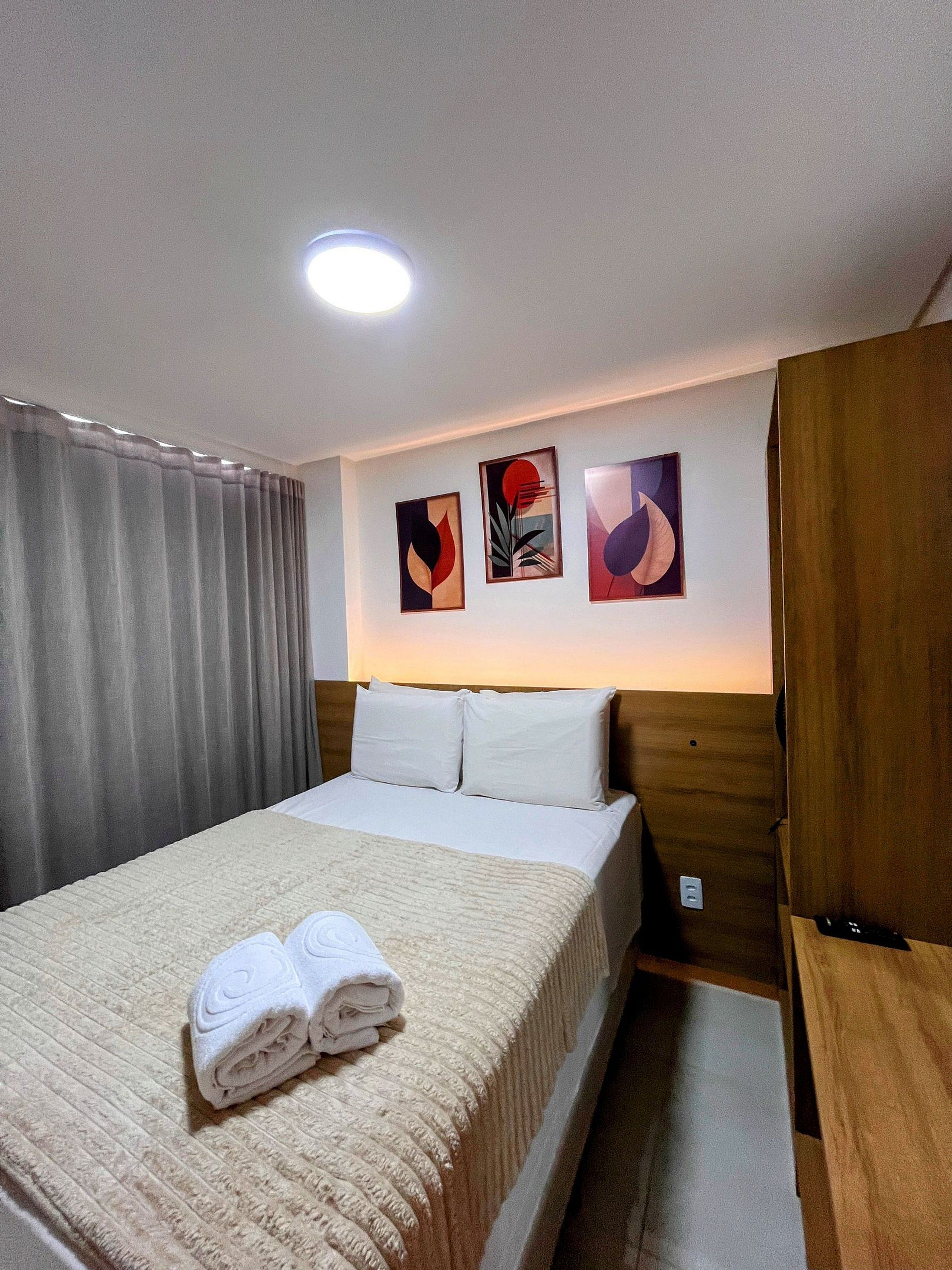 A hotel room with a bed, a wooden wardrobe, and three wall art pieces.