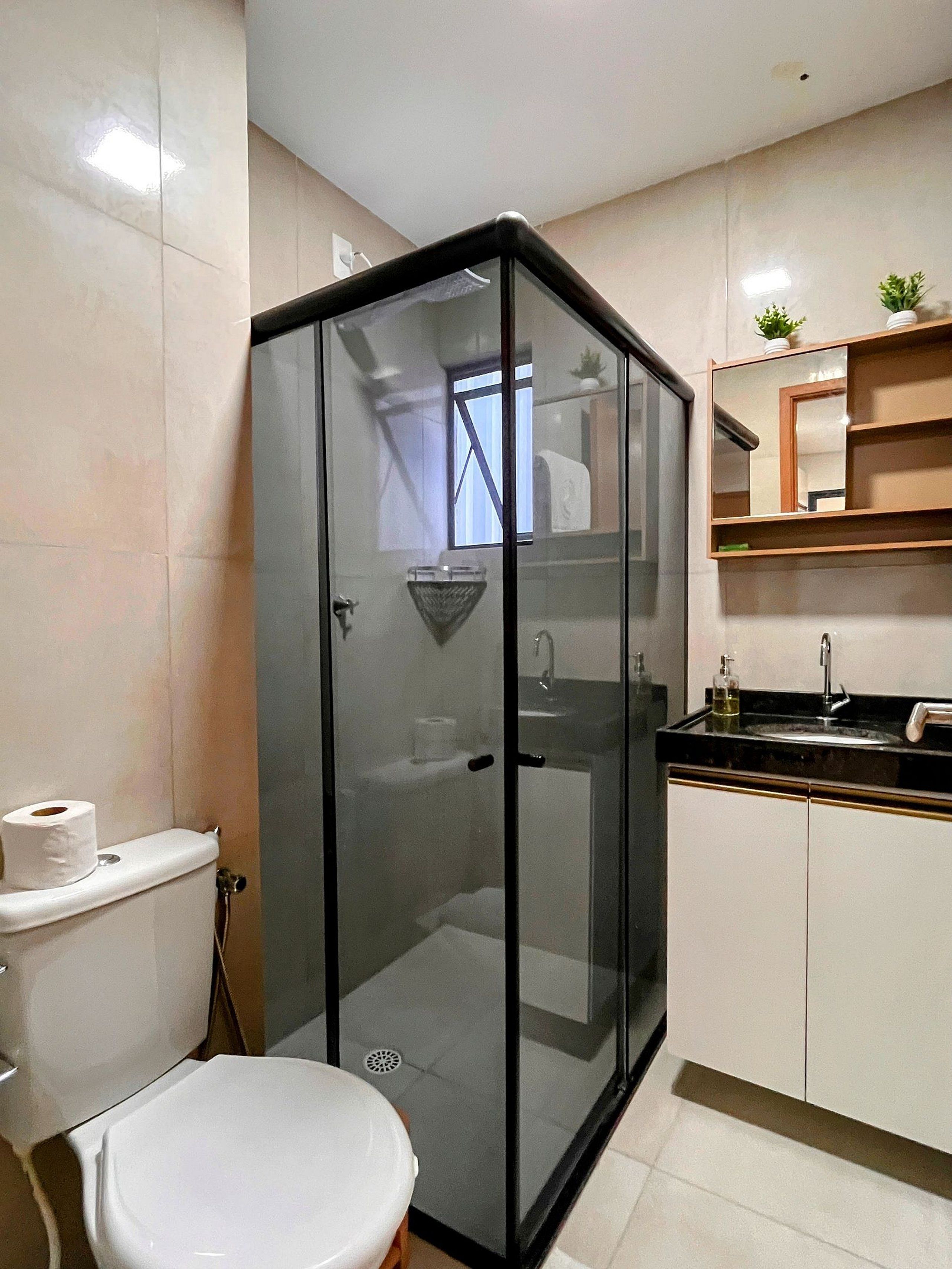 A bathroom with a glass-enclosed shower, a toilet, and a sink with a mirror above it.