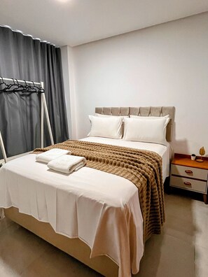 A neatly made bed with a headboard, a bedside table with a lamp, and a window with curtains. - Moana Residencial - VSH (Ipojuca)