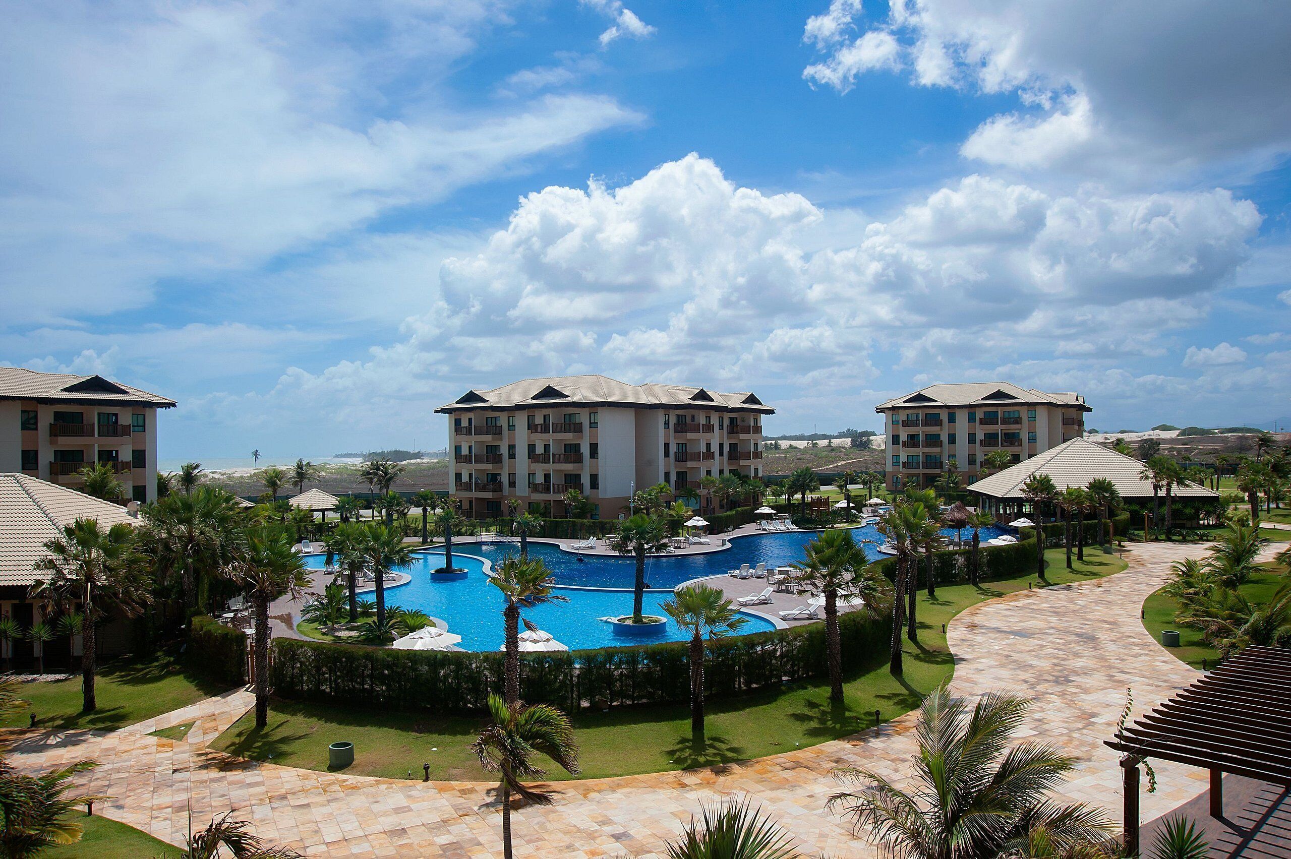 A resort with a central pool, multiple buildings, and palm trees.