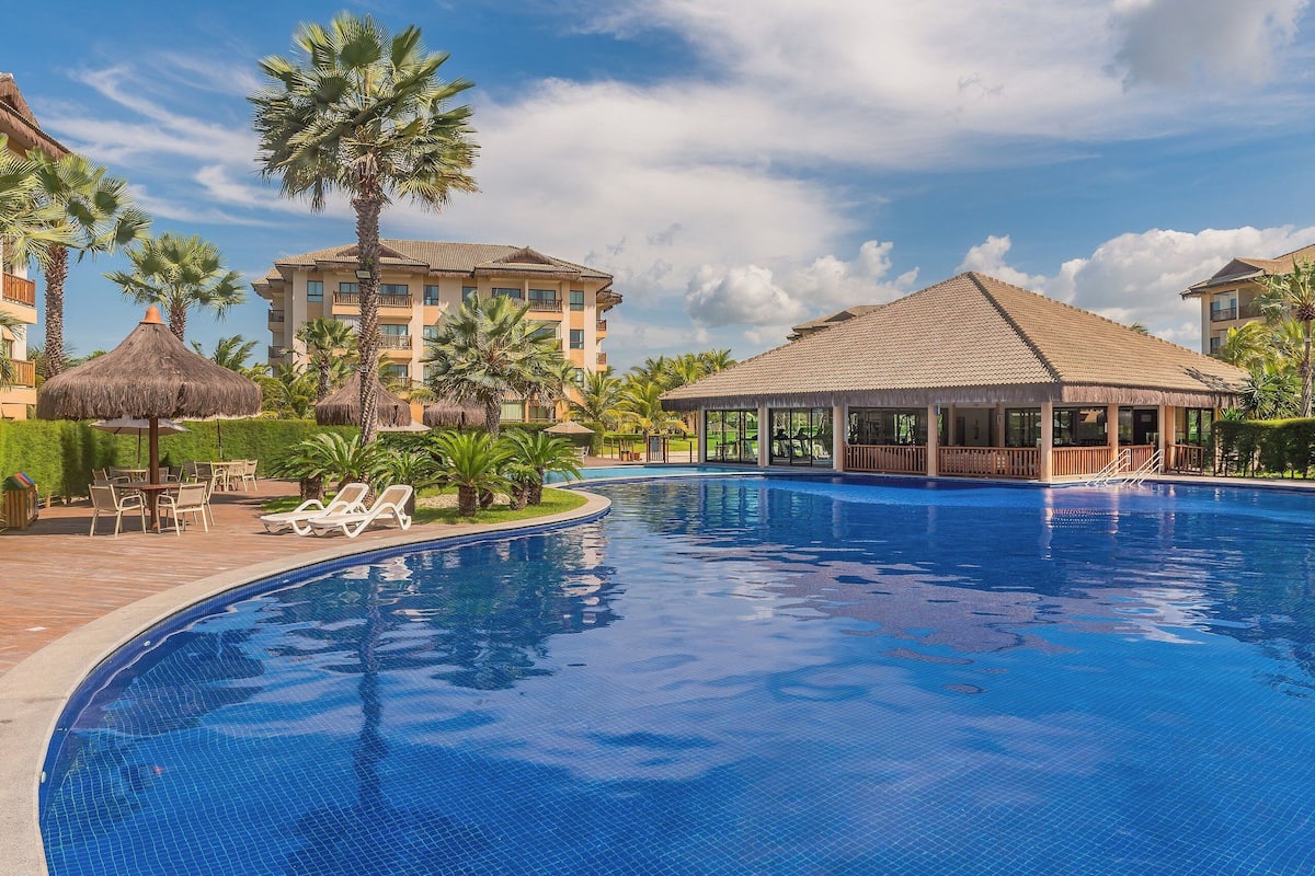 Piscina com espreguiçadeiras, palmeiras e um gazebo.