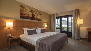 A hotel room with a large bed, two bedside lamps, a nightstand with a phone, a window with curtains, and a painting on the wall.