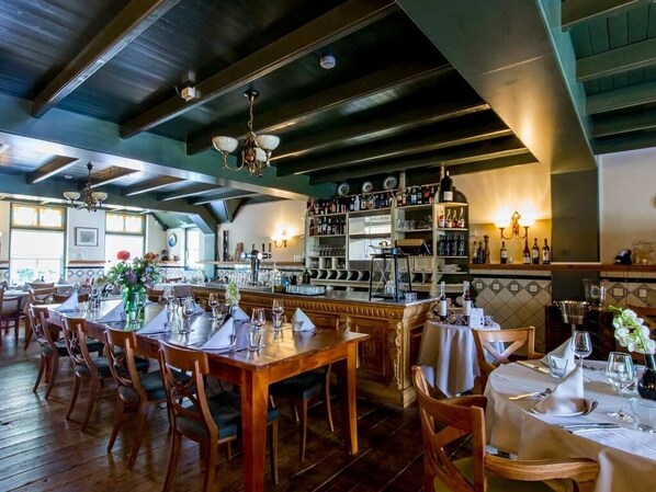 A restaurant with wooden tables and chairs, a bar area with shelves of bottles, and a view of the outdoors.