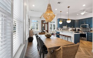 A modern kitchen with dark blue cabinets, stainless steel appliances, and a wooden dining table.