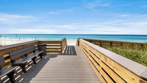 Une promenade en bois menant à une plage, avec un banc et une poubelle.