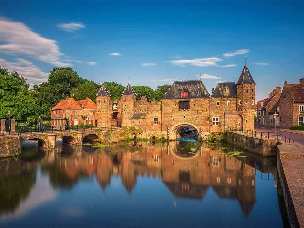 A historic stone building with a moat and a bridge, reflecting in the water.