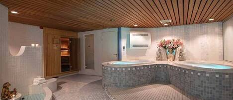 A spa area with a large, curved hot tub, a wooden ceiling, and tiled flooring.