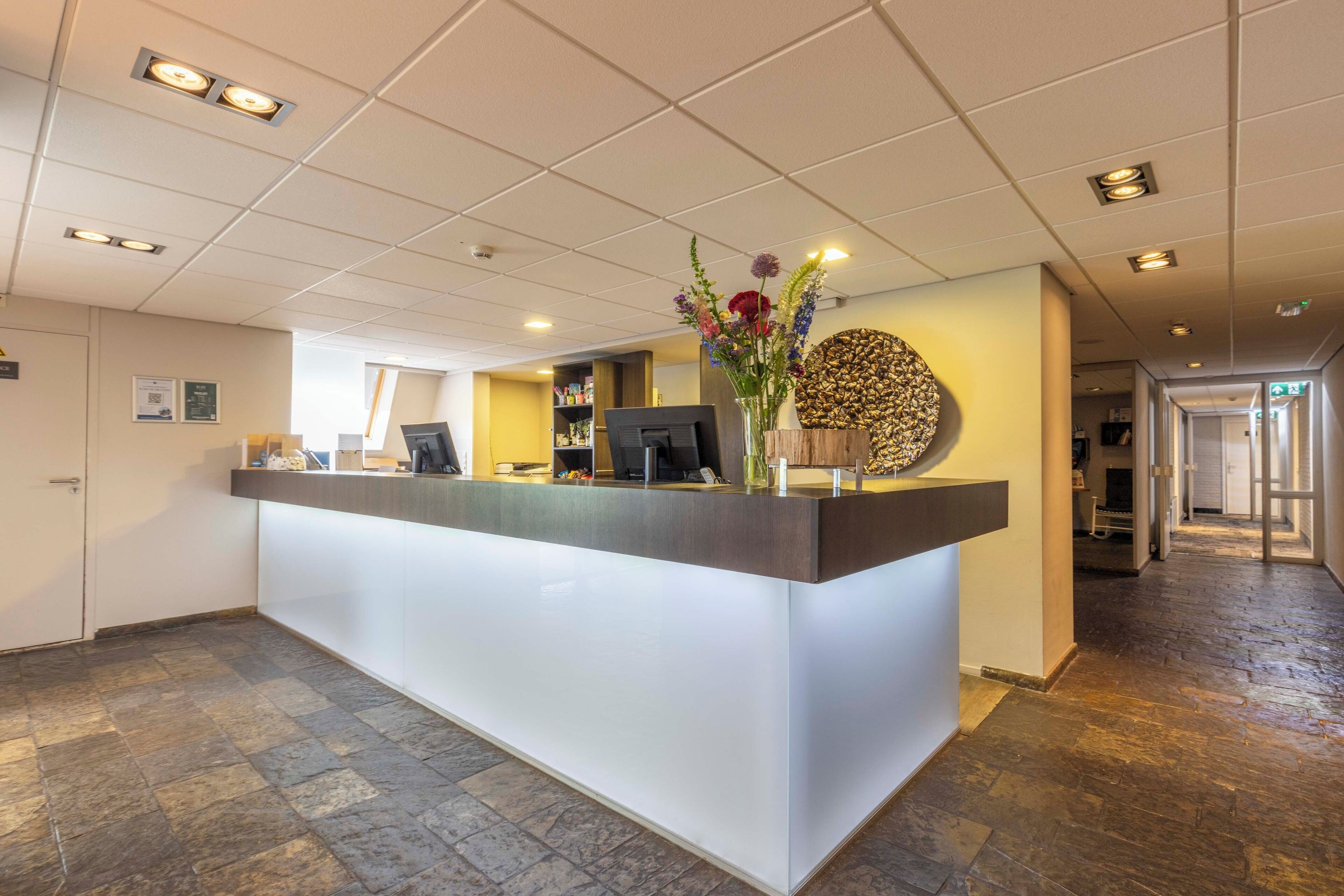 A reception desk with a modern design, a vase with flowers, and a wall-mounted decorative piece.