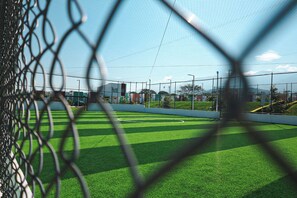 En sportplan omgiven av ett stängsel av sammanlänkade metallkedjor, med byggnader i bakgrunden.