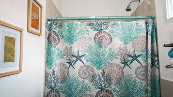 Un baño con cortina de ducha estampada con motivos marinos, una obra de arte enmarcada en la pared y un cabezal de ducha visible.