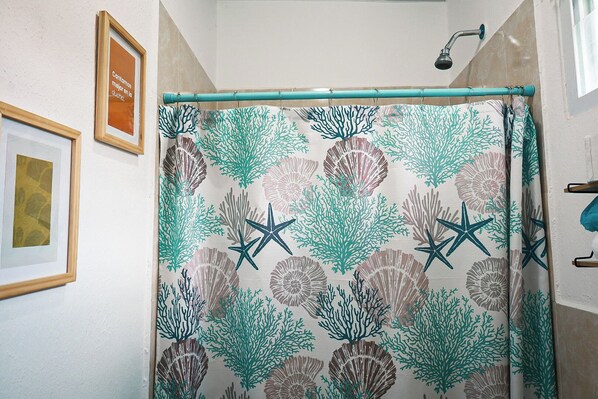 A bathroom with a shower curtain featuring a sea life pattern, framed artwork on the wall, and a visible showerhead. - Casa 88 a 30 minutos de ataco (Ahuachapan)