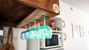 Una cocina con recipientes de vidrio verde colgantes, utensilios de madera, un microondas y una estantería con una lata de pasta.