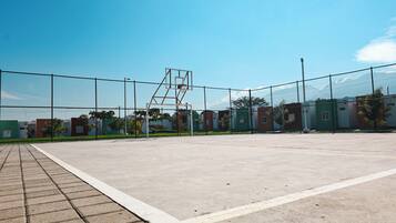 Un campo da basket all'aperto con un canestro in metallo, circondato da una recinzione in rete metallica.