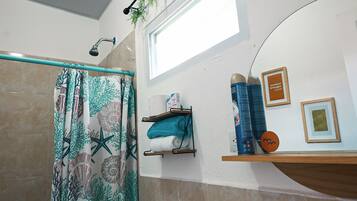 Une salle de bain avec un rideau de douche à motifs marins, un porte-serviettes avec des serviettes et une étagère contenant des articles de toilette.