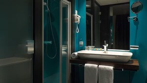 Un baño moderno con cabina de ducha de vidrio, un lavamanos blanco con espejo y dos toallas sobre el mostrador.