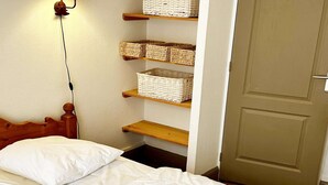 A bedroom with a wooden headboard, a bed with white bedding, and shelves with wicker baskets.