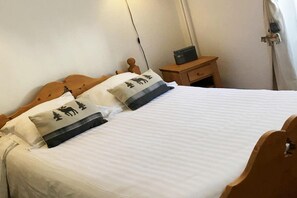 A neatly made bed with two pillows, a wooden headboard, a bedside table with a lamp, and a wall socket. - Romantic Mountain Stay in Mont-Dore (Mont-Dore)