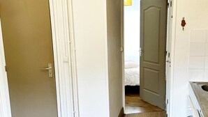 A hallway leading to a bedroom with a bed, a door, and a kitchen area with a sink.