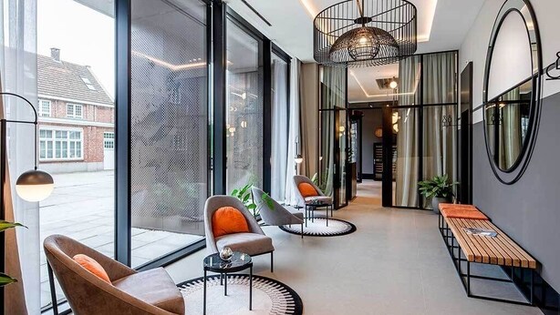 A modern hotel lobby with large windows, a seating area with chairs and a bench, and a round table.