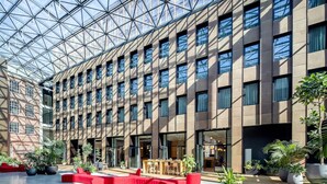 A modern building with a glass ceiling, multiple floors, and a central courtyard with seating and plants.