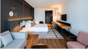 A modern hotel room with a bed, a desk, a TV, and a sofa.