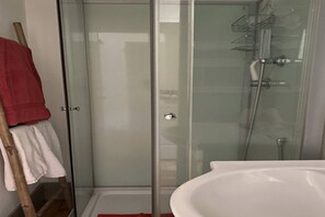 Ein Duschbereich mit Glasabtrennung, ein weißes Waschbecken und ein Handtuchhalter.