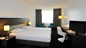 Habitación de hotel con una cama grande, dos mesitas de noche con lámparas, un escritorio con televisor y una silla.