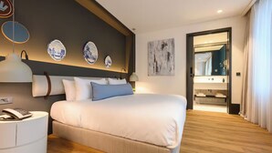 Habitación de hotel moderna con una cama grande, una mesita de noche con teléfono y un baño visible a través de una puerta abierta.