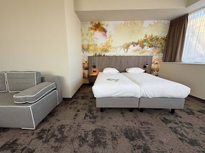 Una habitación de hotel con cama, sofá, mesita de noche y un mural en la pared.