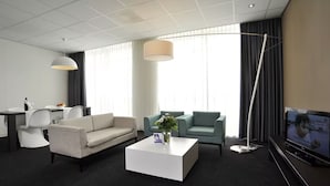 Una habitación de hotel moderna con un sofá blanco, un sofá color crema, una mesa de centro, un televisor y un área de comedor con una mesa y sillas.