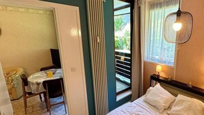 Una camera da letto con un letto, un comodino con una lampada, una finestra con tende, un termosifone e una porta che dà su un balcone.