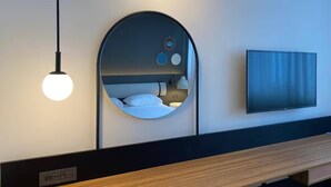 Una habitación de hotel moderna con un espejo circular, un televisor de pantalla plana y un banco de madera.