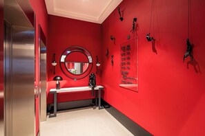 Une pièce aux murs rouges, avec un miroir, un banc et un panneau fixé au mur indiquant les équipements disponibles.