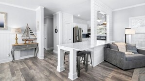 Eine moderne Küche mit weißen Schränken, einer zentralen Kochinsel mit Hockern und einem grauen Sofa in einem Wohnbereich.