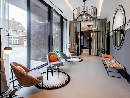 A modern hotel lobby with large windows, a seating area with chairs and a bench, and a round table.