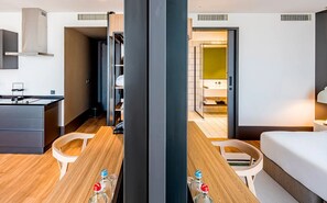 A modern hotel room with a wooden dining table, a bed, a small kitchenette, and a bathroom visible through an open door. - Stylish Forest-Edge Home — Convenient Trail Access, Kitchenette, & Free Parking (Oisterwijk)