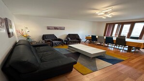 A modern living room with a black sofa, two armchairs, a coffee table, and a dining area with a wooden table and chairs. - Spacious Family Stayin Mont-Dore (Mont-Dore)