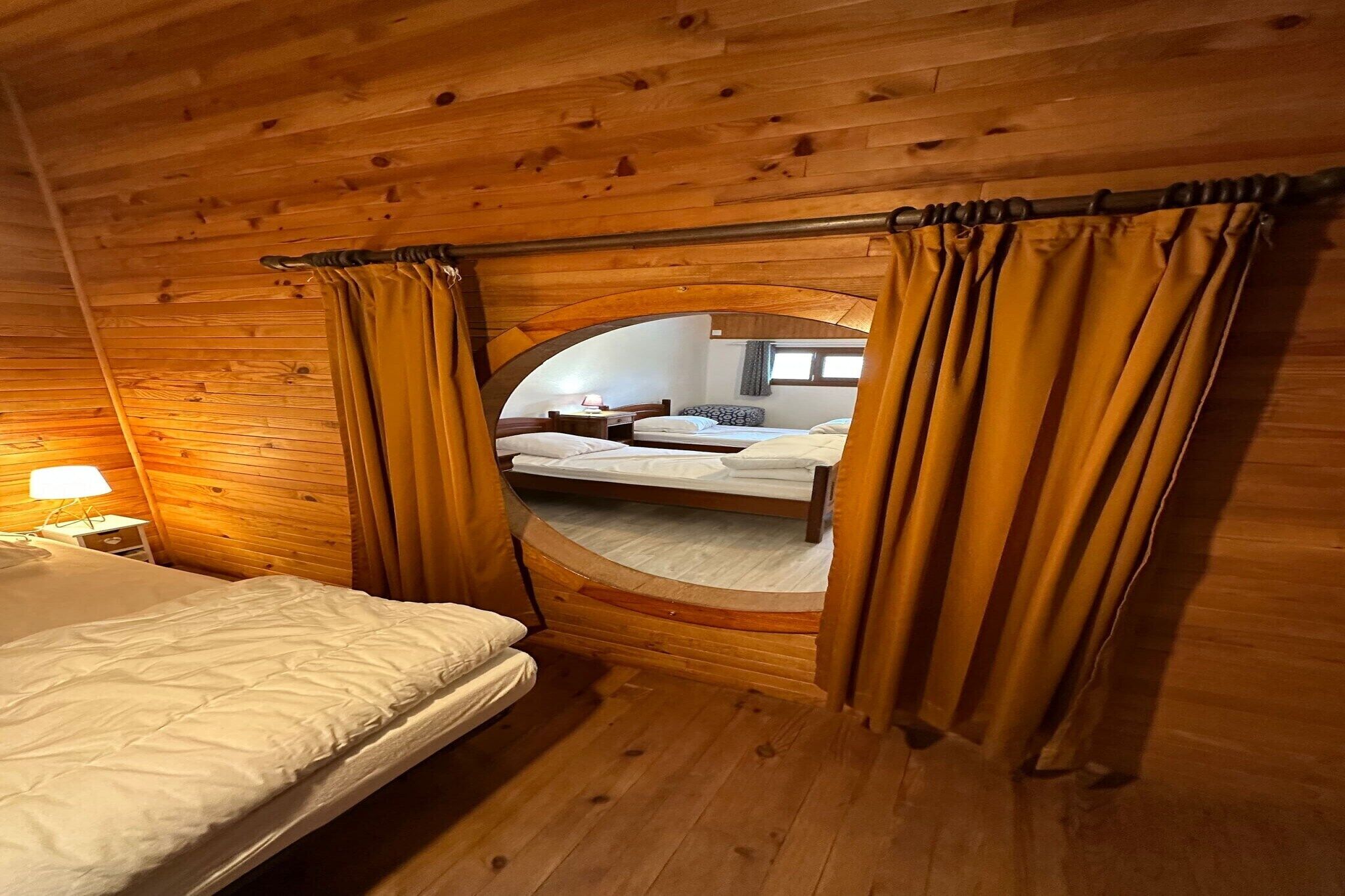 Una habitación de cabaña de madera con una cama, una mesita de noche y un ventanal circular con cortinas.