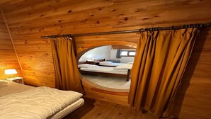 A wooden cabin room with a bed, a nightstand, and a circular window with curtains. - Spacious Family Stayin Mont-Dore (Mont-Dore)